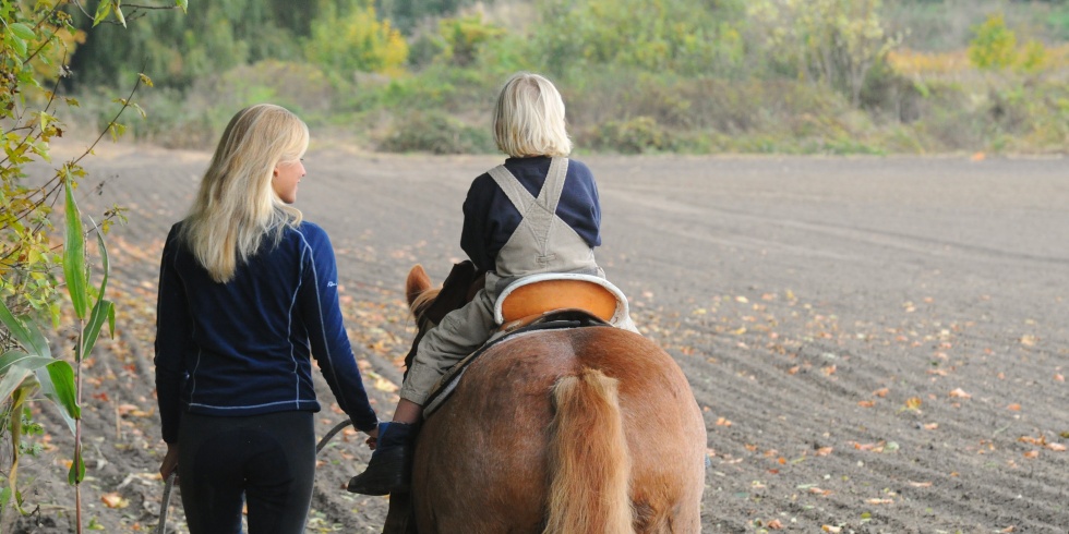Eine junge Frau führt ein Pony mit einem Kind auf seinem Rücken.