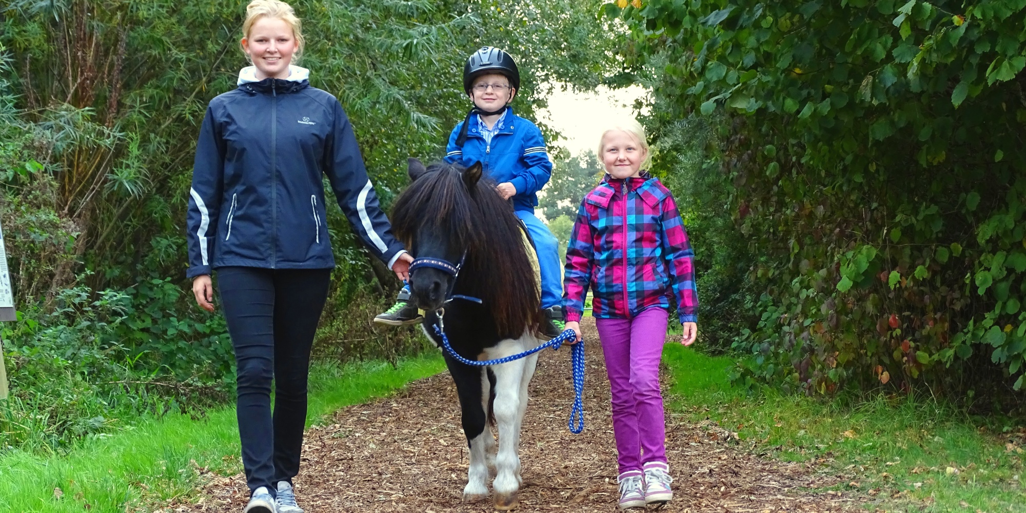 Kinder und Jugendliche führen ein Pony mit einem kleinen Reiter auf seinem Rücken
